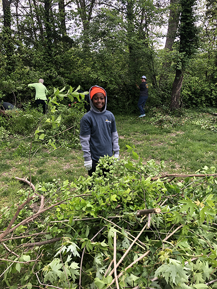 A young boy in an orange hat smiles while standing hear a big pile of branches
